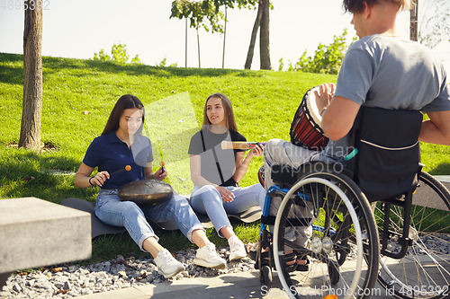 Image of Happy handicapped man on a wheelchair spending time with friends playing live instrumental music outdoors