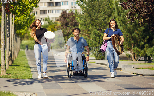 Image of Happy handicapped man on a wheelchair spending time with friends playing live instrumental music outdoors