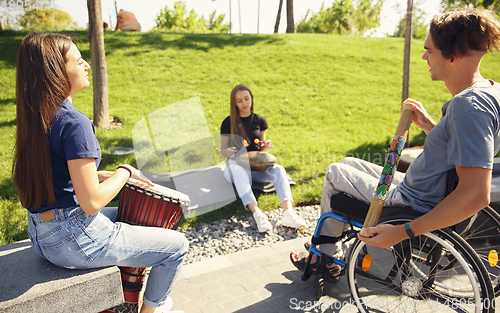 Image of Happy handicapped man on a wheelchair spending time with friends playing live instrumental music outdoors