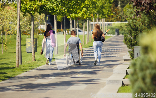 Image of Happy handicapped man on a wheelchair spending time with friends playing live instrumental music outdoors