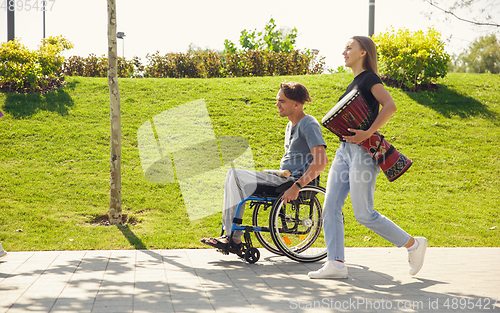 Image of Happy handicapped man on a wheelchair spending time with friends playing live instrumental music outdoors