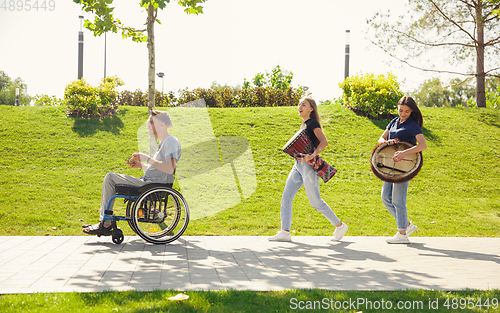 Image of Happy handicapped man on a wheelchair spending time with friends playing live instrumental music outdoors