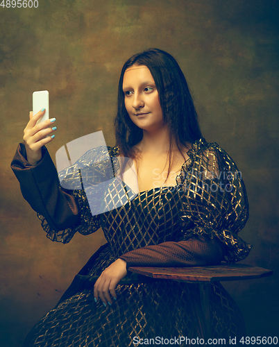 Image of Young woman as Mona Lisa on dark background. Retro style, comparison of eras concept.