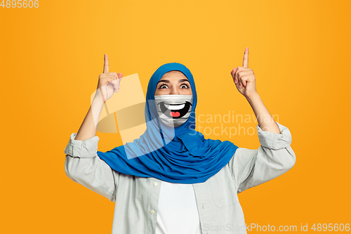 Image of Portrait of young girl with emotion on her protective face mask isolated on studio background. Beautiful female model, funny expression