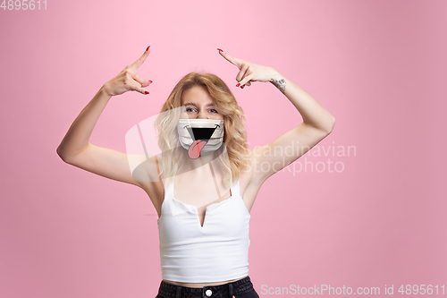 Image of Portrait of young girl with emotion on her protective face mask isolated on studio background. Beautiful female model, funny expression