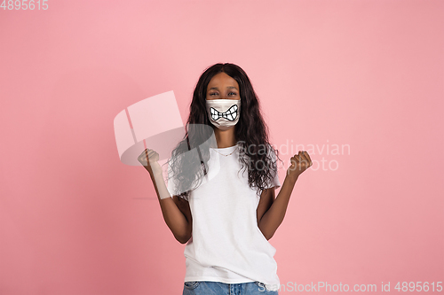 Image of Portrait of young girl with emotion on her protective face mask isolated on studio background. Beautiful female model, funny expression