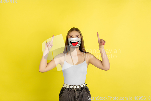 Image of Portrait of young girl with emotion on her protective face mask isolated on studio background. Beautiful female model, funny expression