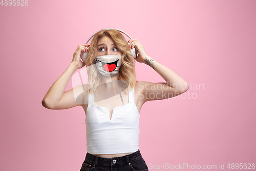 Image of Portrait of young girl with emotion on her protective face mask isolated on studio background. Beautiful female model, funny expression