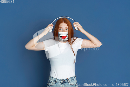 Image of Portrait of young girl with emotion on her protective face mask isolated on studio background. Beautiful female model, funny expression