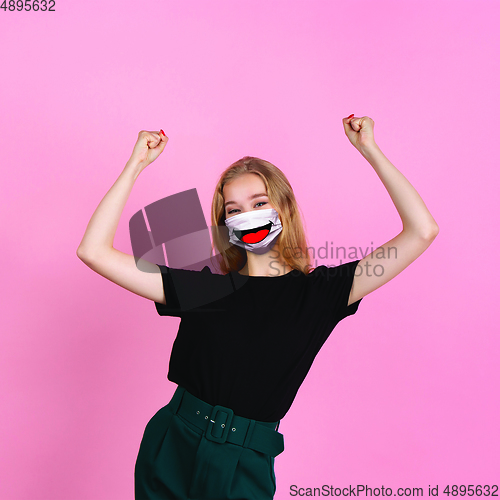 Image of Portrait of young girl with emotion on her protective face mask isolated on studio background. Beautiful female model, funny expression