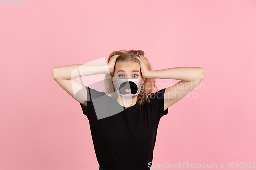 Image of Portrait of young girl with emotion on her protective face mask isolated on studio background. Beautiful female model, funny expression