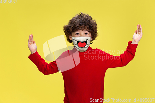 Image of Portrait of little boy with emotion on his protective face mask isolated on studio background. Beautiful male model, funny expression