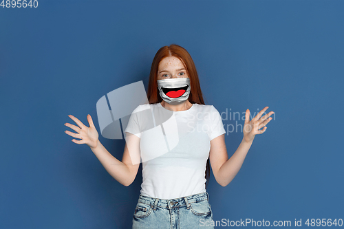 Image of Portrait of young girl with emotion on her protective face mask isolated on studio background. Beautiful female model, funny expression