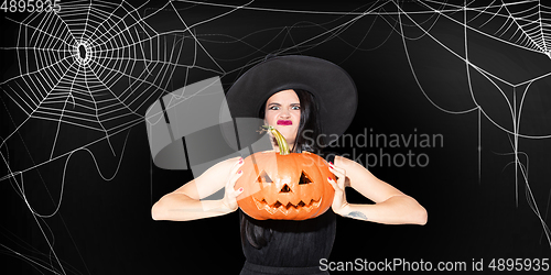 Image of Young woman in hat as a witch on scary black background