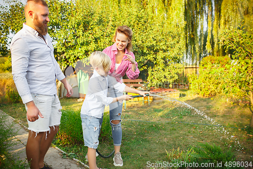 Image of Happy family during watering plants in a garden outdoors. Love, family, lifestyle, harvest concept.
