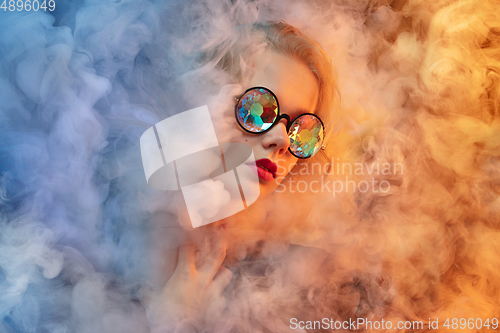 Image of Young beautiful woman on neon colored studio background in smoke cloud. Human emotions, facial expression, beauty concept.