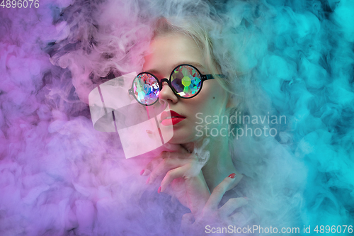 Image of Young beautiful woman on neon colored studio background in smoke cloud. Human emotions, facial expression, beauty concept.