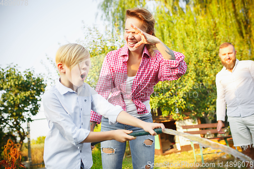 Image of Happy family during watering plants in a garden outdoors. Love, family, lifestyle, harvest concept.