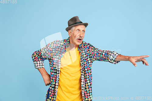 Image of Senior hipster man in stylish hat isolated on blue background. Tech and joyful elderly lifestyle concept