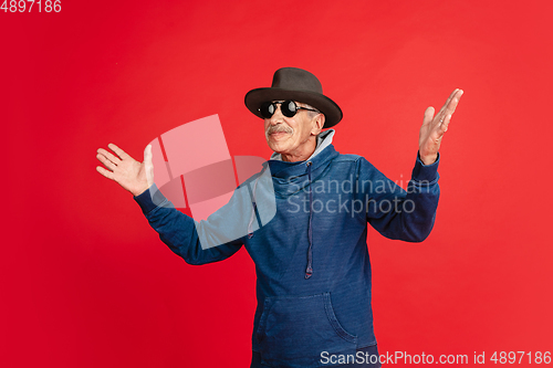 Image of Senior man in stylish eyewear and hat isolated on red background. Tech and joyful elderly lifestyle concept