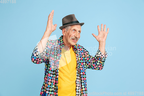 Image of Senior hipster man in stylish hat isolated on blue background. Tech and joyful elderly lifestyle concept