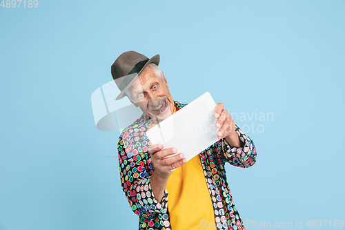 Image of Senior hipster man in stylish hat isolated on blue background. Tech and joyful elderly lifestyle concept