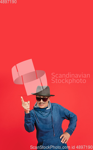 Image of Senior man in stylish eyewear and hat isolated on red background. Tech and joyful elderly lifestyle concept