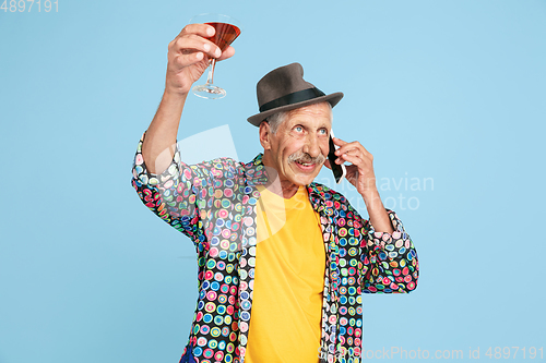 Image of Senior hipster man in stylish hat isolated on blue background. Tech and joyful elderly lifestyle concept