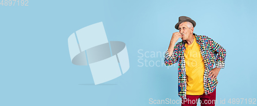 Image of Senior hipster man in stylish hat isolated on blue background. Tech and joyful elderly lifestyle concept