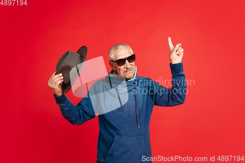 Image of Senior man in stylish eyewear and hat isolated on red background. Tech and joyful elderly lifestyle concept