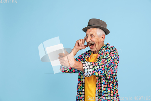 Image of Senior hipster man in stylish hat isolated on blue background. Tech and joyful elderly lifestyle concept