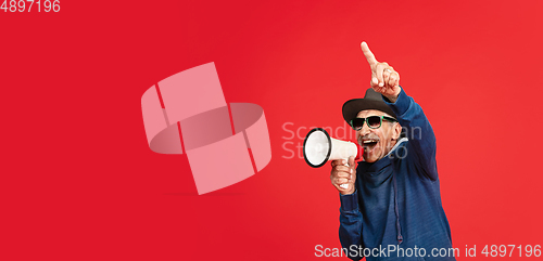 Image of Senior man in stylish eyewear and hat isolated on red background. Tech and joyful elderly lifestyle concept