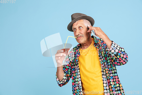 Image of Senior hipster man in stylish hat isolated on blue background. Tech and joyful elderly lifestyle concept