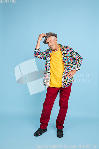 Image of Senior hipster man in stylish hat isolated on blue background. Tech and joyful elderly lifestyle concept