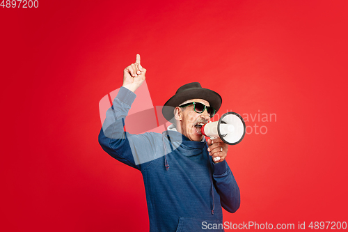 Image of Senior man in stylish eyewear and hat isolated on red background. Tech and joyful elderly lifestyle concept