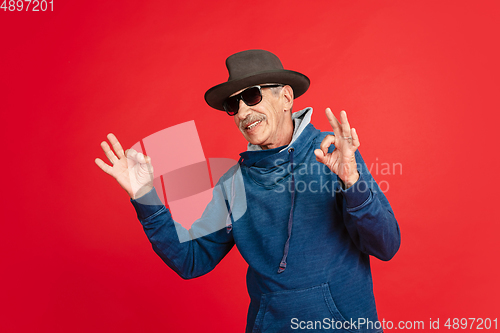 Image of Senior man in stylish eyewear and hat isolated on red background. Tech and joyful elderly lifestyle concept