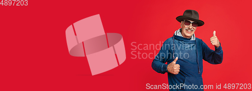 Image of Senior man in stylish eyewear and hat isolated on red background. Tech and joyful elderly lifestyle concept