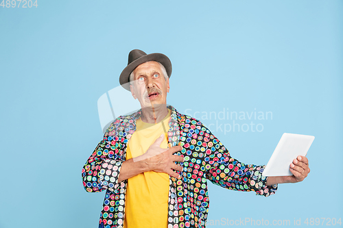 Image of Senior hipster man in stylish hat isolated on blue background. Tech and joyful elderly lifestyle concept
