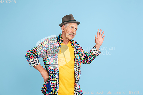 Image of Senior hipster man in stylish hat isolated on blue background. Tech and joyful elderly lifestyle concept