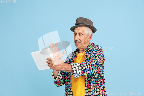 Image of Senior hipster man in stylish hat isolated on blue background. Tech and joyful elderly lifestyle concept