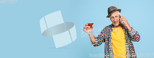 Image of Senior hipster man in stylish hat isolated on blue background. Tech and joyful elderly lifestyle concept