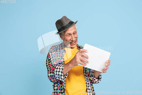 Image of Senior hipster man in stylish hat isolated on blue background. Tech and joyful elderly lifestyle concept