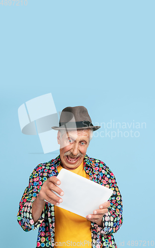 Image of Senior hipster man in stylish hat isolated on blue background. Tech and joyful elderly lifestyle concept