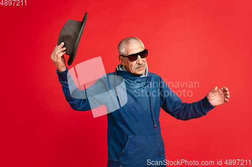 Image of Senior man in stylish eyewear and hat isolated on red background. Tech and joyful elderly lifestyle concept