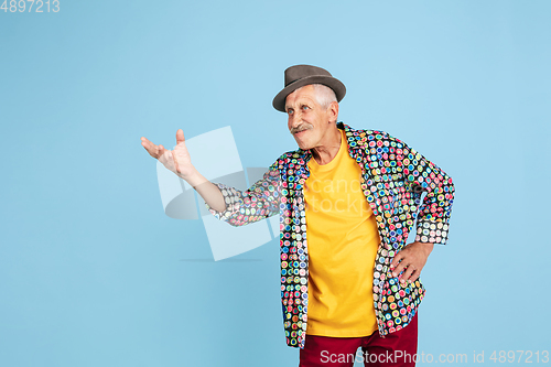 Image of Senior hipster man in stylish hat isolated on blue background. Tech and joyful elderly lifestyle concept