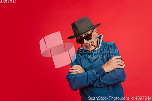 Image of Senior man in stylish eyewear and hat isolated on red background. Tech and joyful elderly lifestyle concept