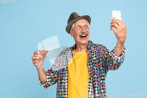 Image of Senior hipster man in stylish hat isolated on blue background. Tech and joyful elderly lifestyle concept