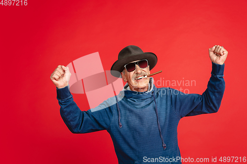 Image of Senior man in stylish eyewear and hat isolated on red background. Tech and joyful elderly lifestyle concept