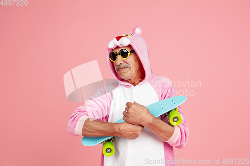 Image of Senior hipster man in stylish pink attire isolated on pink background. Tech and joyful elderly lifestyle concept