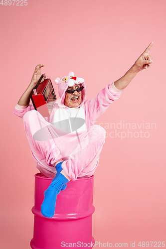 Image of Senior hipster man in stylish pink attire isolated on pink background. Tech and joyful elderly lifestyle concept